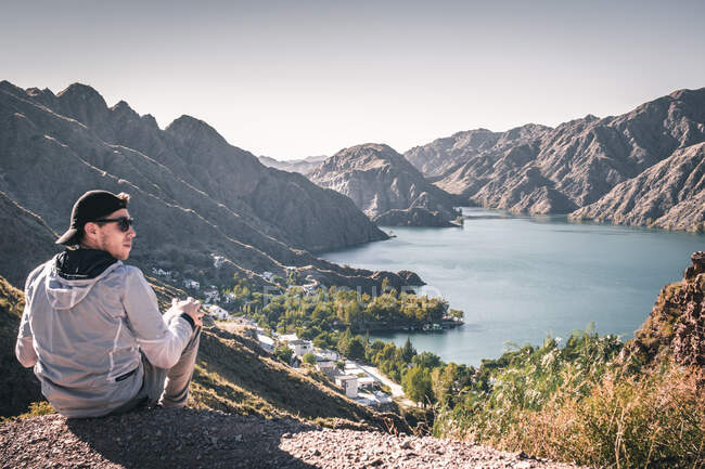 Man in cap sitting on a cliff in front of a water reservoir — Stock Photo