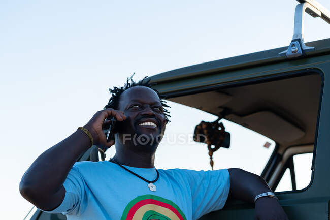 Черный мужчина средних лет улыбается, разговаривая по телефону в своей зеленой машине — стоковое фото
