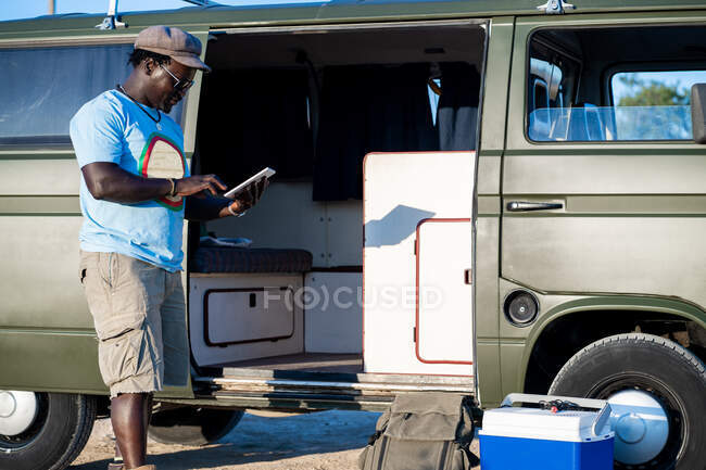 Hombre afroamericano escribiendo en la tableta en un camping - foto de stock