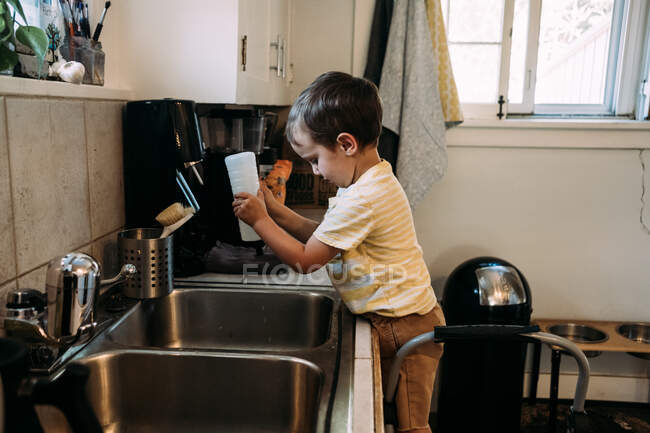 Kleiner Junge spielt mit Spritzflasche an Küchenspüle — Stockfoto