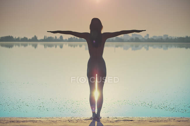 Оголена жінка стоїть біля річки з простягнутими руками на світанку . — стокове фото