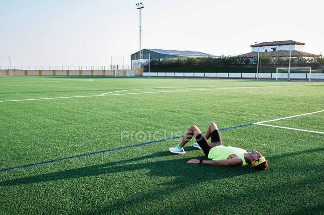 Jovem descansando na grama de um campo de futebol após o treinamento — Fotografia de Stock