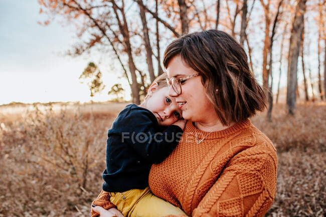 Felice madre che abbraccia il suo contenuto bambino in una calda serata autunnale — Foto stock