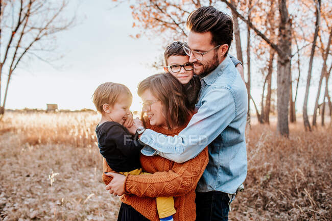 Fashionable young family hugging in a field on a cool autumn evening — Stock Photo