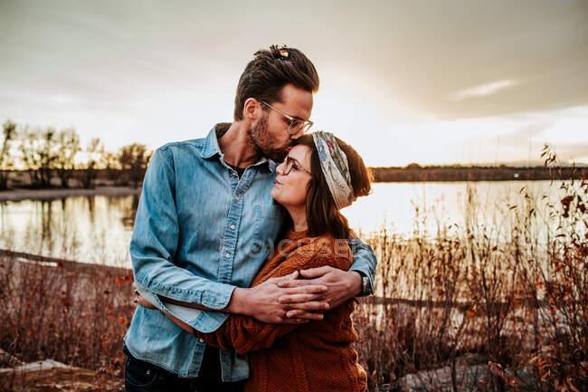 Модный муж целует улыбающуюся жену возле озера в Колорадо — стоковое фото