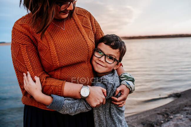 Mamma abbracciare giovane figlio sulla riva di un lago in una sera d'autunno — Foto stock