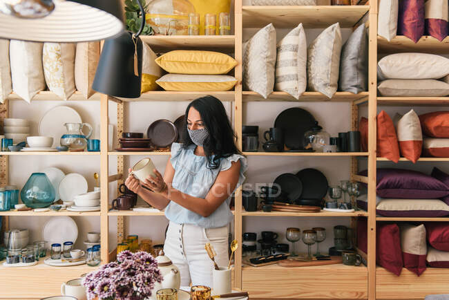 Жінка з масками, що тримають кавову чашку ручної роботи в магазині. — стокове фото