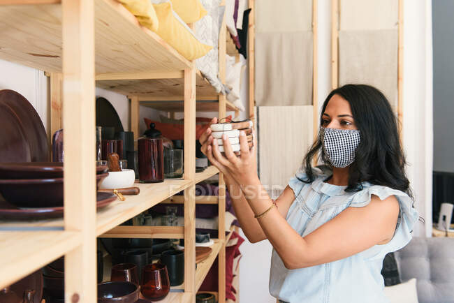 Femme masquée inspectant les dessous de verre dans un magasin de produits de luxe — Photo de stock