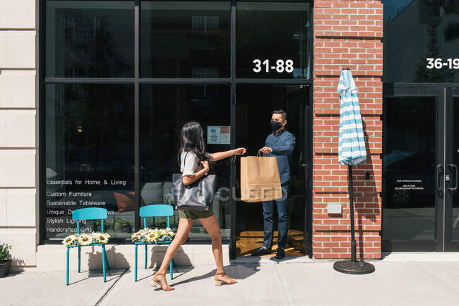 Femme stylisée ramassage paquet au bord de la rue du propriétaire d'entreprise masqué — Photo de stock
