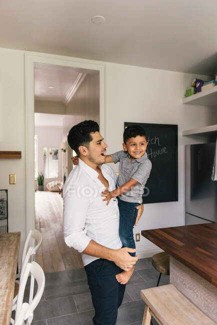 Father holding young son in arm in kitchen and laughing together — Stock Photo