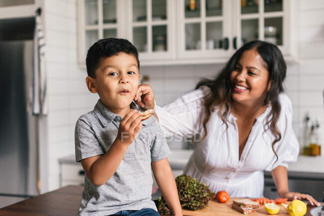 Madre e figlio si divertono insieme mentre mangiano panini in cucina — Foto stock
