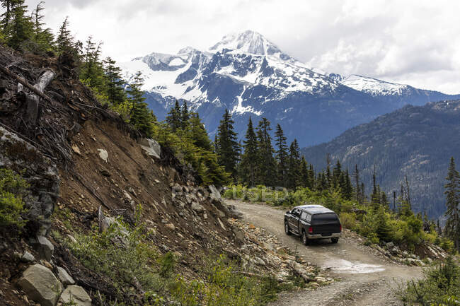 Modern vehicle driving along curvy logging road near rough slope during trip through snowy mountains in British Columbia, Canada — Stock Photo