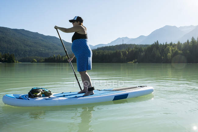 Вагітна жінка верхи на дошці СУП на гірському озері — стокове фото