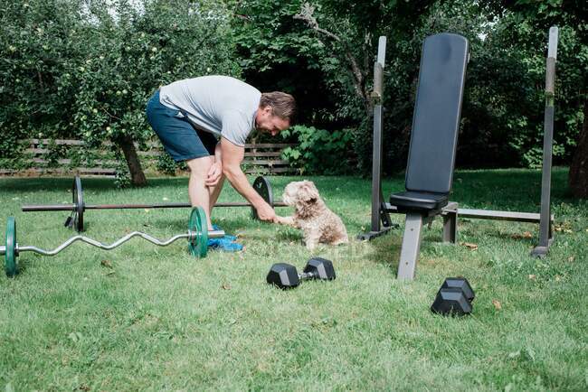 Man holding his dogs paw whilst working out at home in quarantine — Stock Photo