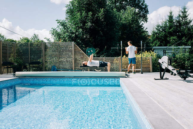 Deux hommes travaillant ensemble au bord de la piscine à la salle de gym à domicile — Photo de stock