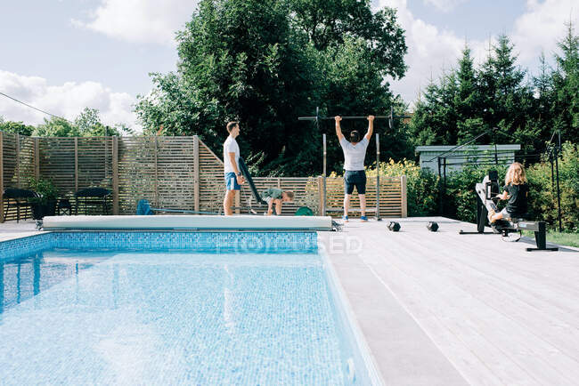 Due uomini e i loro figli si allenano nella palestra di casa a bordo piscina — Foto stock