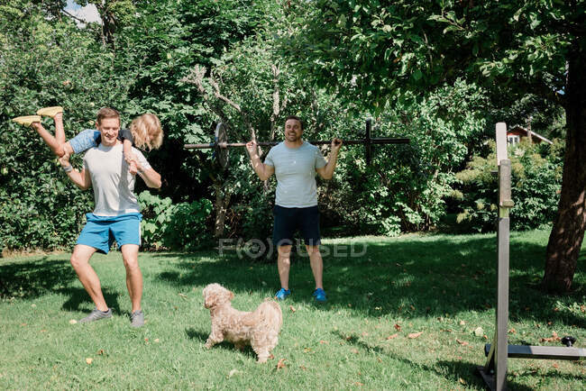 Two men working out together at home with their children and dog — Stock Photo
