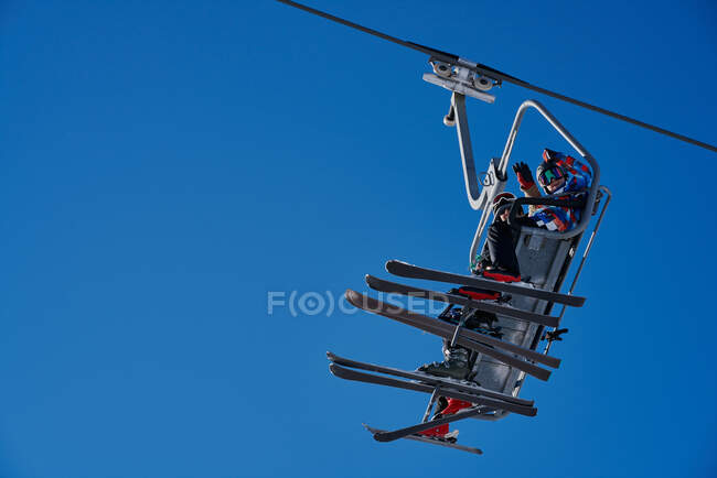 Skieurs sur un télésiège regardant vers le bas avec un fond bleu — Photo de stock