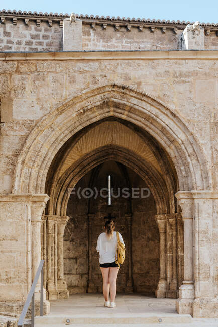 Menina olhando para o arco de uma igreja com uma mochila — Fotografia de Stock