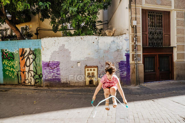Young girl playing with a skipping rope in a colorful street — Stock Photo