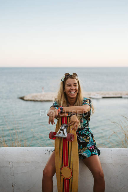 Laughing female with long board skate in front of Mediterranean sea — Stock Photo