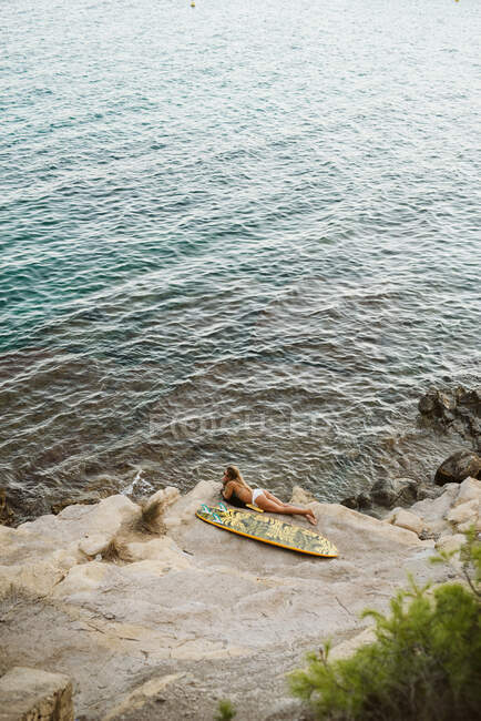 Surfista femenina acostada con tabla de surf naranja en la pequeña bahía de Moraira - foto de stock