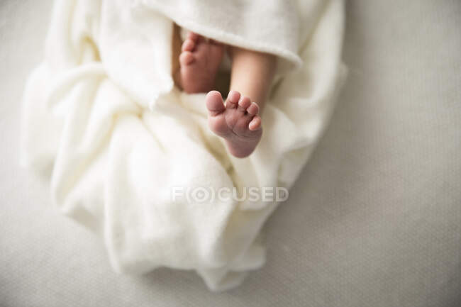 Закройте ноги новорожденному младенцу, завернутому в белое одеяло — стоковое фото