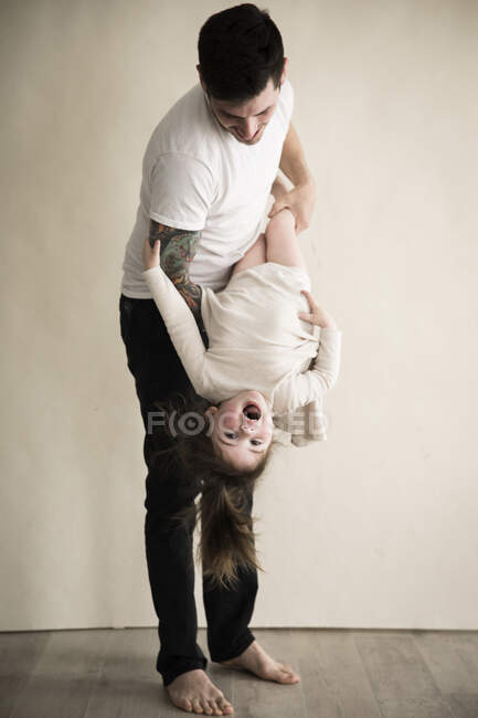Feliz tatuado millennial papá sostiene niño hija al revés abajo - foto de stock