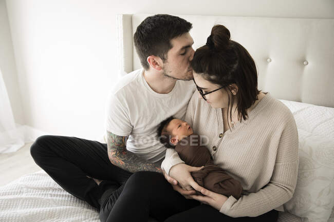 Tatuado Millennial pai beija a mãe enquanto ela mantém seu recém-nascido — Fotografia de Stock
