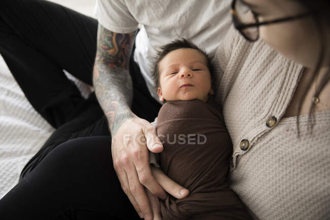 Garçon nouveau-né emmailloté en brun, tenu par les parents tatoués Hipster — Photo de stock