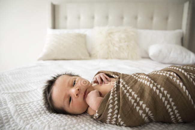 Nouveau-né avec beaucoup de couches de cheveux foncés emmaillotées sur le lit à la maison — Photo de stock