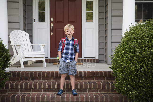 Grinsender blonder Junge mit den Händen in den Taschen steht auf Ziegelsteinen — Stockfoto