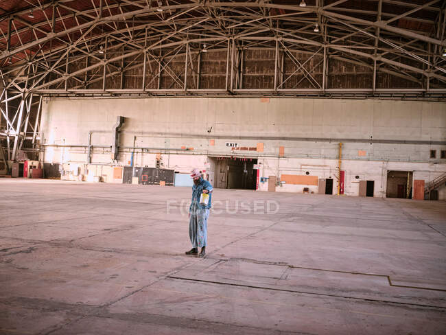A man dressed in denim holds a can of paint in a large airplane hanger — Stock Photo