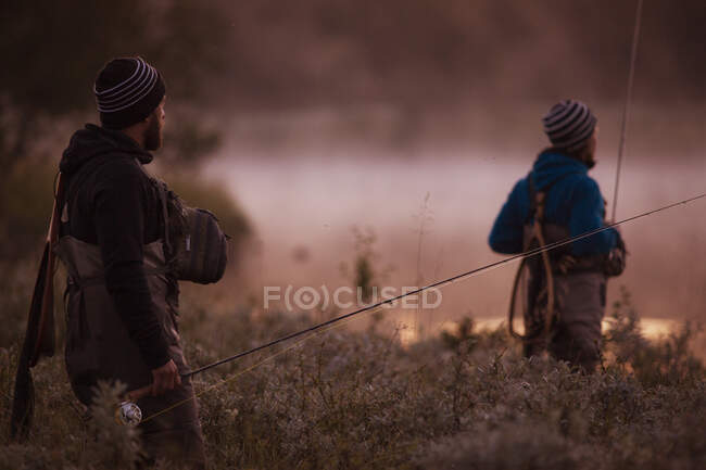 Dos pescadores mosca mirando el río en la niebla de la mañana - foto de stock