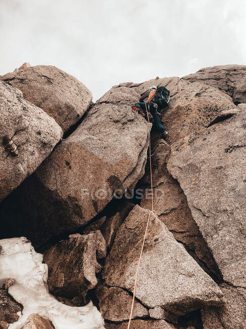 Climber ascending steep rock face with crampons secured by rope — Stock Photo