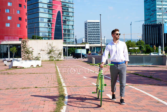 Bearded man in sunglasses walking with bike by bicycle track outdoors — Stock Photo