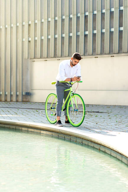 Retrato al aire libre del joven guapo con teléfono móvil y bicicleta de engranaje fijo en la calle. - foto de stock