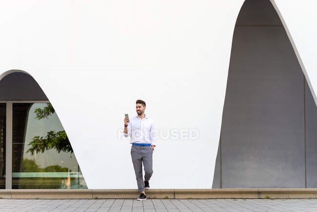 Young bearded man leaning against a white wall using the mobile phone — Stock Photo