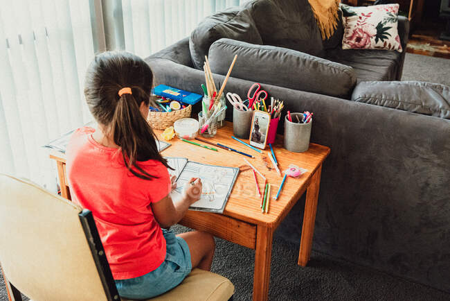 Multi razziale 8 anno vecchio ragazza seduta a scrivania colorazione & faccia tempistica — Foto stock