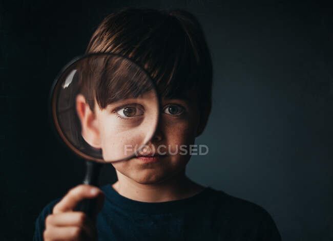 Porträt eines kleinen Jungen, der eine Lupe über ein Auge hält — Stockfoto