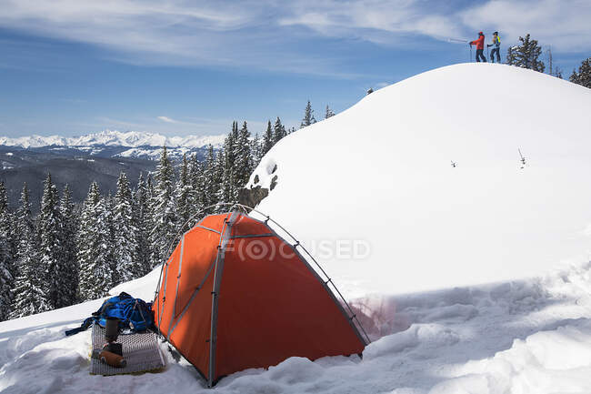 Caminhante masculino e feminino em pé na montanha coberta de neve enquanto tenda em primeiro plano — Fotografia de Stock