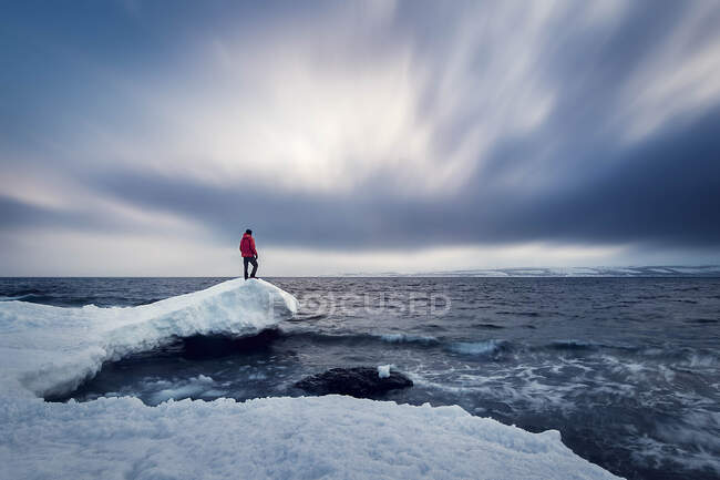 Homem de pé na neve coberta de rocha por mar contra o céu nublado — Fotografia de Stock