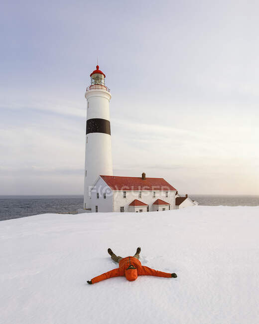 Male hiker relaxing on snow covered mountain while lighthouse in background — Stock Photo