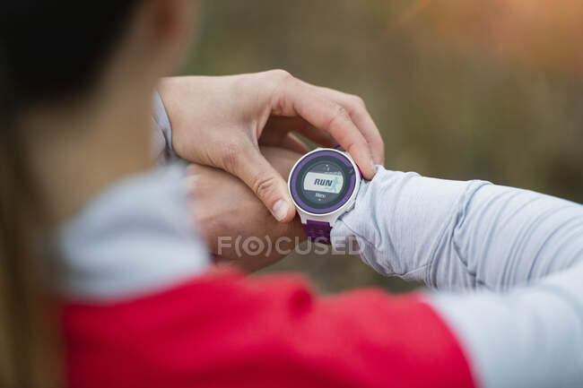 Mujer comprobando el tiempo en reloj de pulsera mientras corre en el bosque - foto de stock