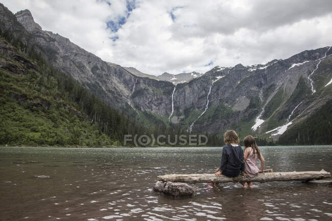 Діти сидять на дереві в гірському озері — стокове фото