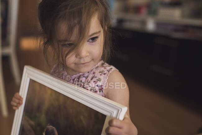 Sweet brown-eyed 4 yr old girl with wispy hair holding framed picture — Stock Photo