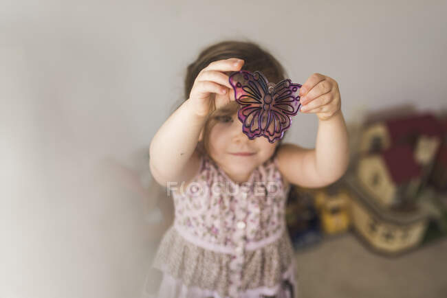 4 yr old girl in sleeveless dress examining butterfly suncatcher — Stock Photo
