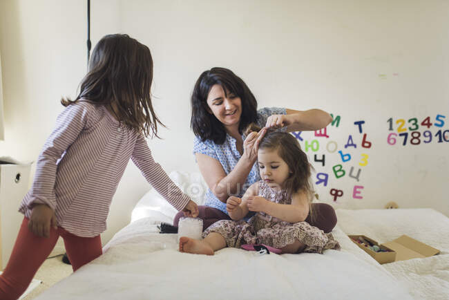 Mother combing 4 yr old daughter's hair while 6 yr old sister watches — Stock Photo