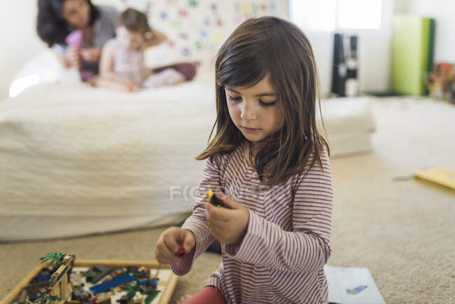 Junges altes Mädchen trägt gestreiftes Hemd auf dem Boden und spielt mit Legos — Stockfoto