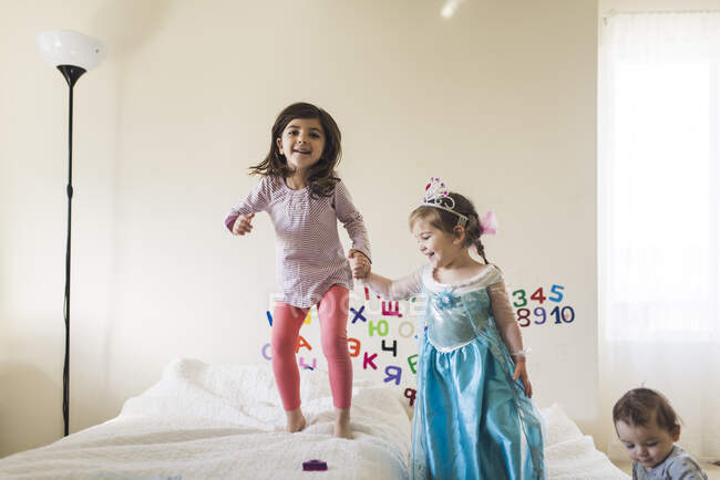 Rire 6 ans fille et 4 ans en robe de princesse sautant sur le lit — Photo de stock